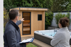 Deux personnes inspectent un sauna en bois près d'un spa
